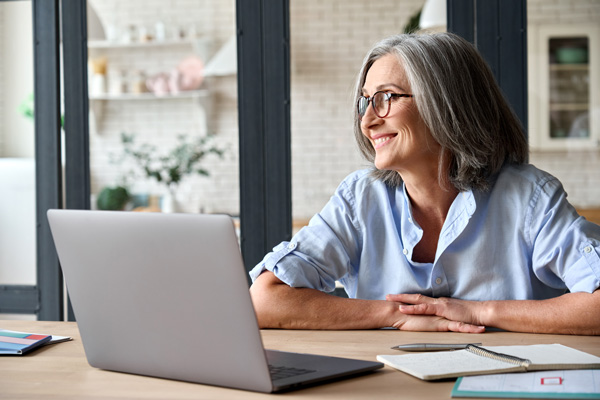 Image of a happy older woman sitting at a desk with a laptop computer.